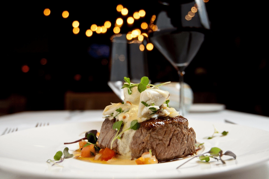 steak covered in sauce on a white plate at a fancy restaurant with a glass of red wine 